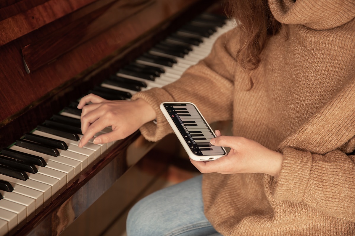 Mulher aprendendo a tocar piano usando aplicativo em seu celular Mulher aprendendo a tocar piano usando aplicativo em seu celular